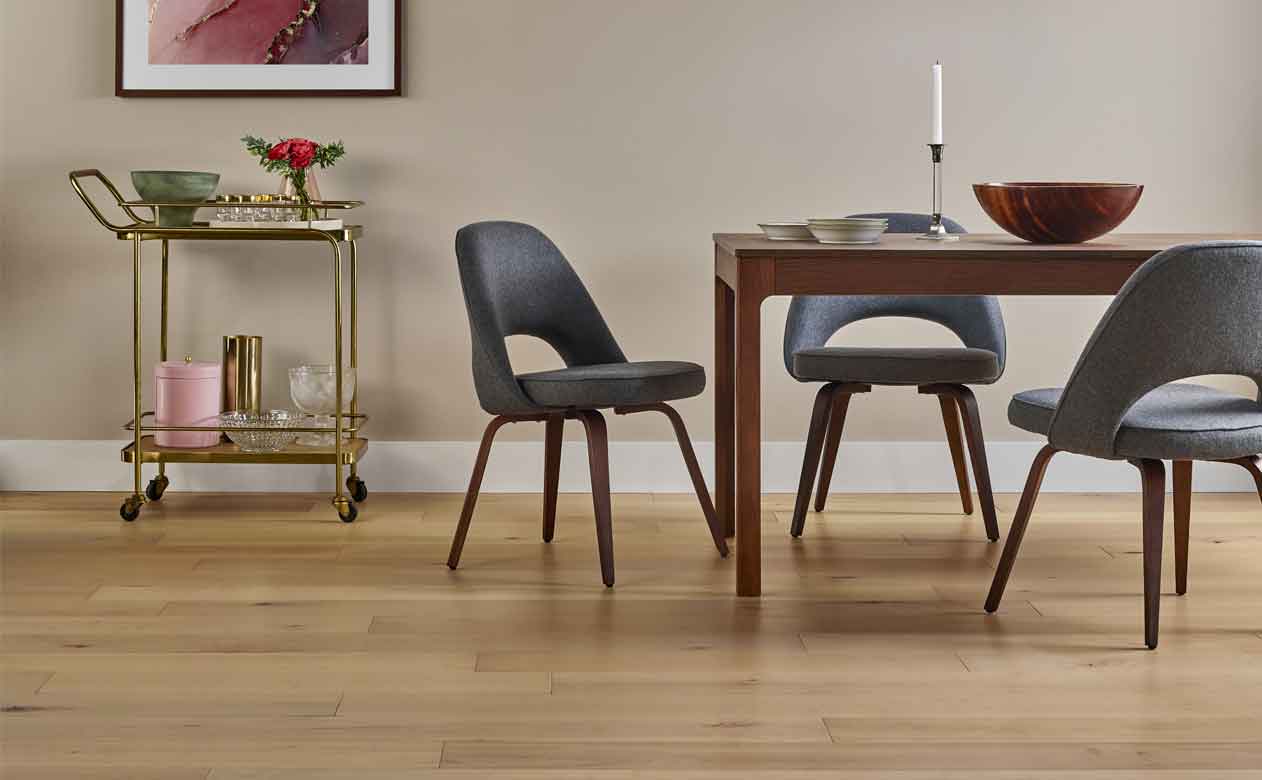 light toned hardwood in dining room with wood table, gold bar cart and gray chairs